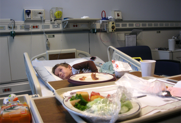 Photo of young boy with eczema in hospital bed with tray of food