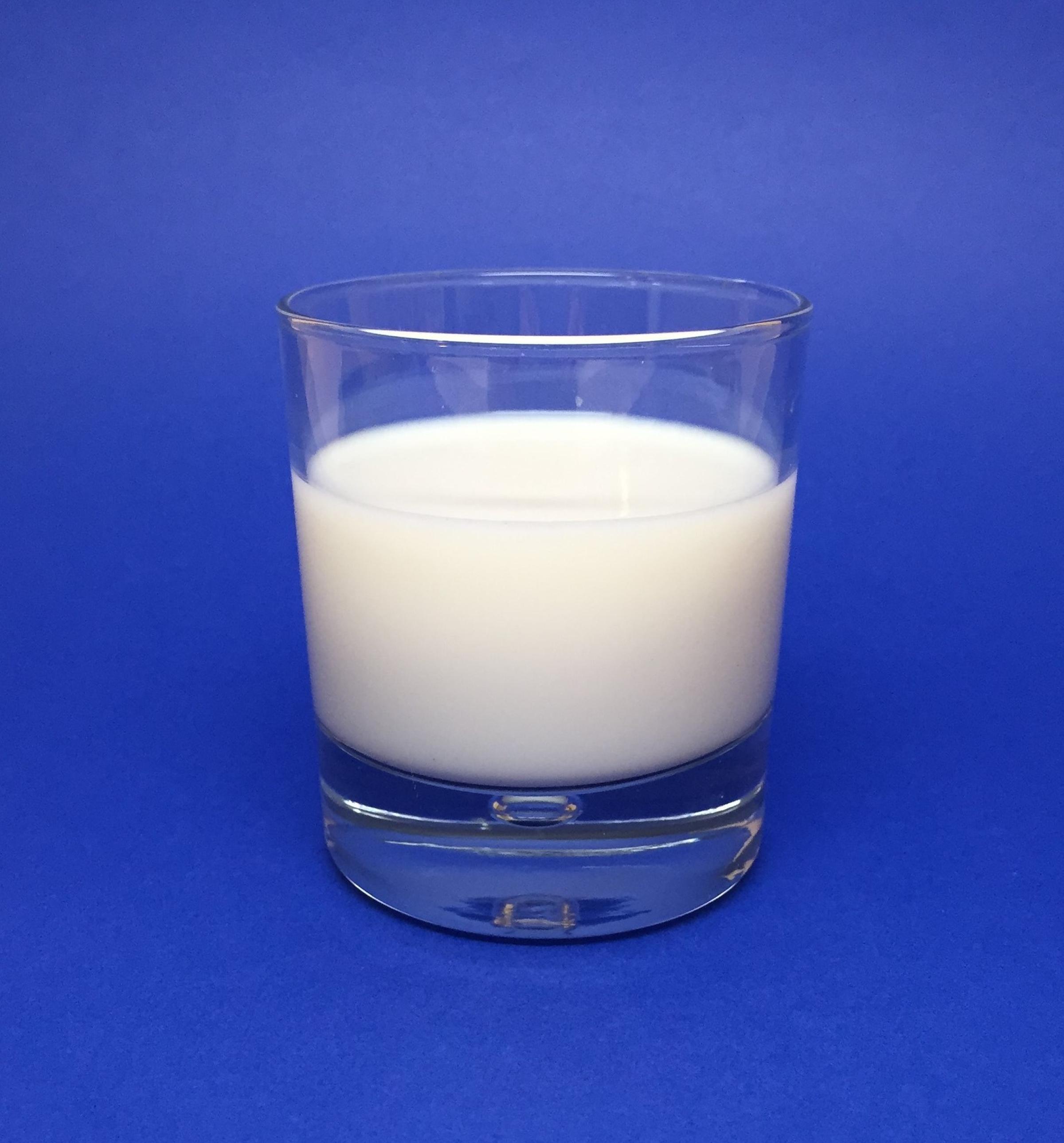 Clear glass of milk on blue background.