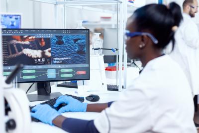 A researcher in a laboratory looks at a computer screen displaying DNA data.