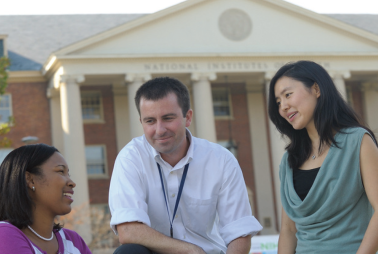 Three people gather in front of the NIH.