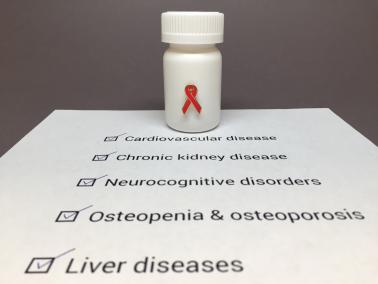 Pill bottle with a red HIV awareness ribbon sitting on a piece of paper listing of HIV comorbidities: cardiovascular disease, chronic kidney disease, neurocognitive disorders, osteopenia and osteoporosis, and liver diseases. 
