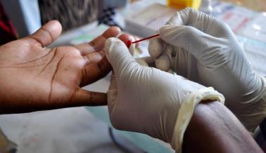 Close-up of blood from an adult’s finger being captured in a capillary tube for an HIV test