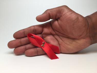 A man’s hand holding an HIV awareness ribbon