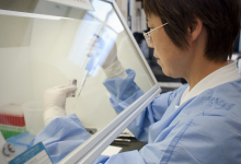 NIAID Vaccine Research Center scientist uses pipetting tool under fume hood in lab.