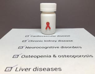 Pill bottle with a red HIV awareness ribbon sitting on a piece of paper listing of HIV comorbidities: cardiovascular disease, chronic kidney disease, neurocognitive disorders, osteopenia and osteoporosis, and liver diseases. 