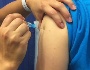 hand injects needle of syringe into shoulder muscle
