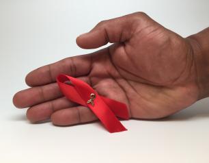 A man’s hand holding an HIV awareness ribbon