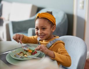 A smiling child eats a meal at a table.