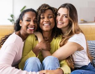 Photo of three young women smiling and embracing