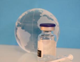 an empty vaccine vial and syringe sit in front of a glass globe