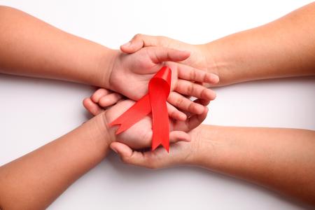 Close up photo of woman's hand and child's hand holding red ribbon together.