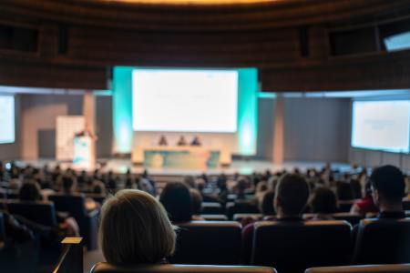 long view from the back of a filled auditorium of a screen and speaker