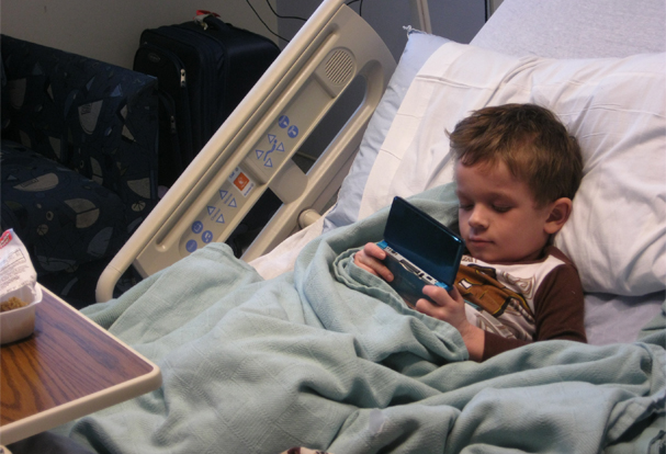 Boy eczema patient plays video game in bed.